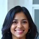 professional headshot of a smiling south asian woman in her late 20s with long dark hair, wearing a colorful blouse, neutral background